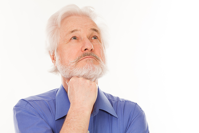 A imagem exibe um homem idoso, de cabelos, barba e bigode brancos, e olhos azuis, em posição de dúvida. Ele veste uma camisa azul e está com o punho apoiado abaixo do queixo enquanto seu olhar está voltado para cima. O fundo da imagem é branco.